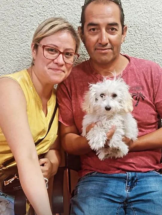 Una pareja sonriente sostiene a su perrito blanco de pelo crespo